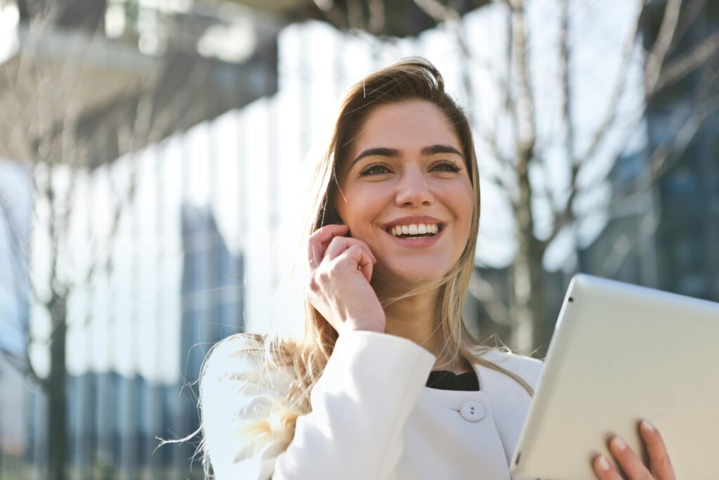Social Media Management Health Brand Tech Confident businesswoman using her tablet and phone, smiling outdoors in sunlight.